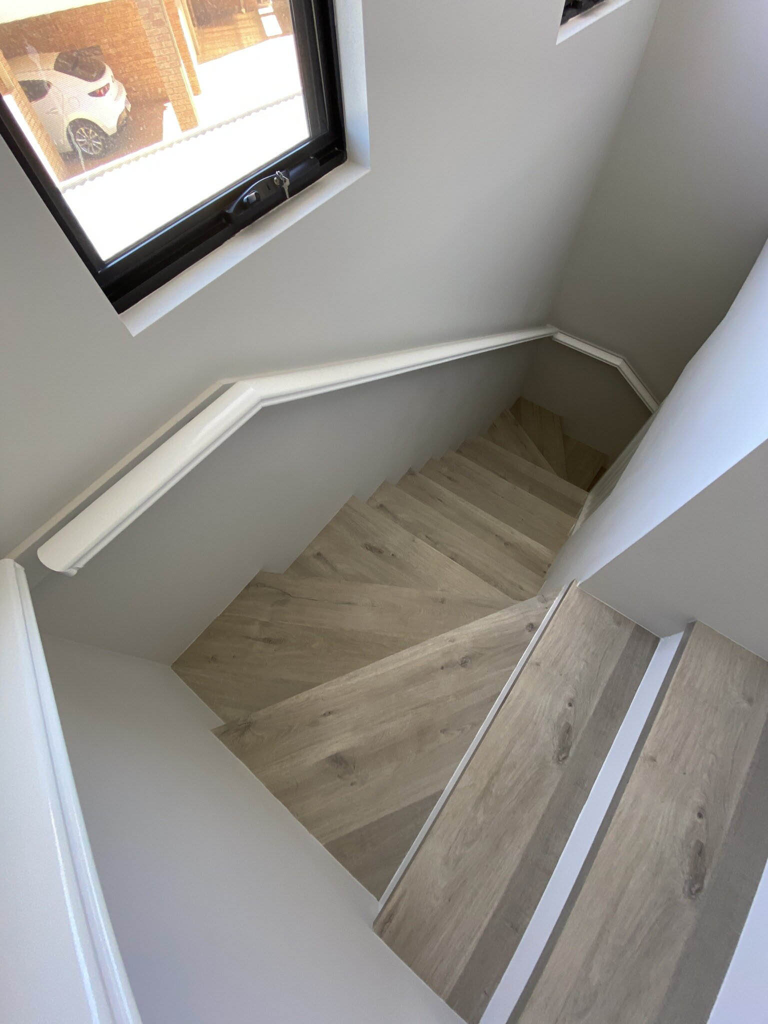 Light timber-look stair treads and white handrail seen from above