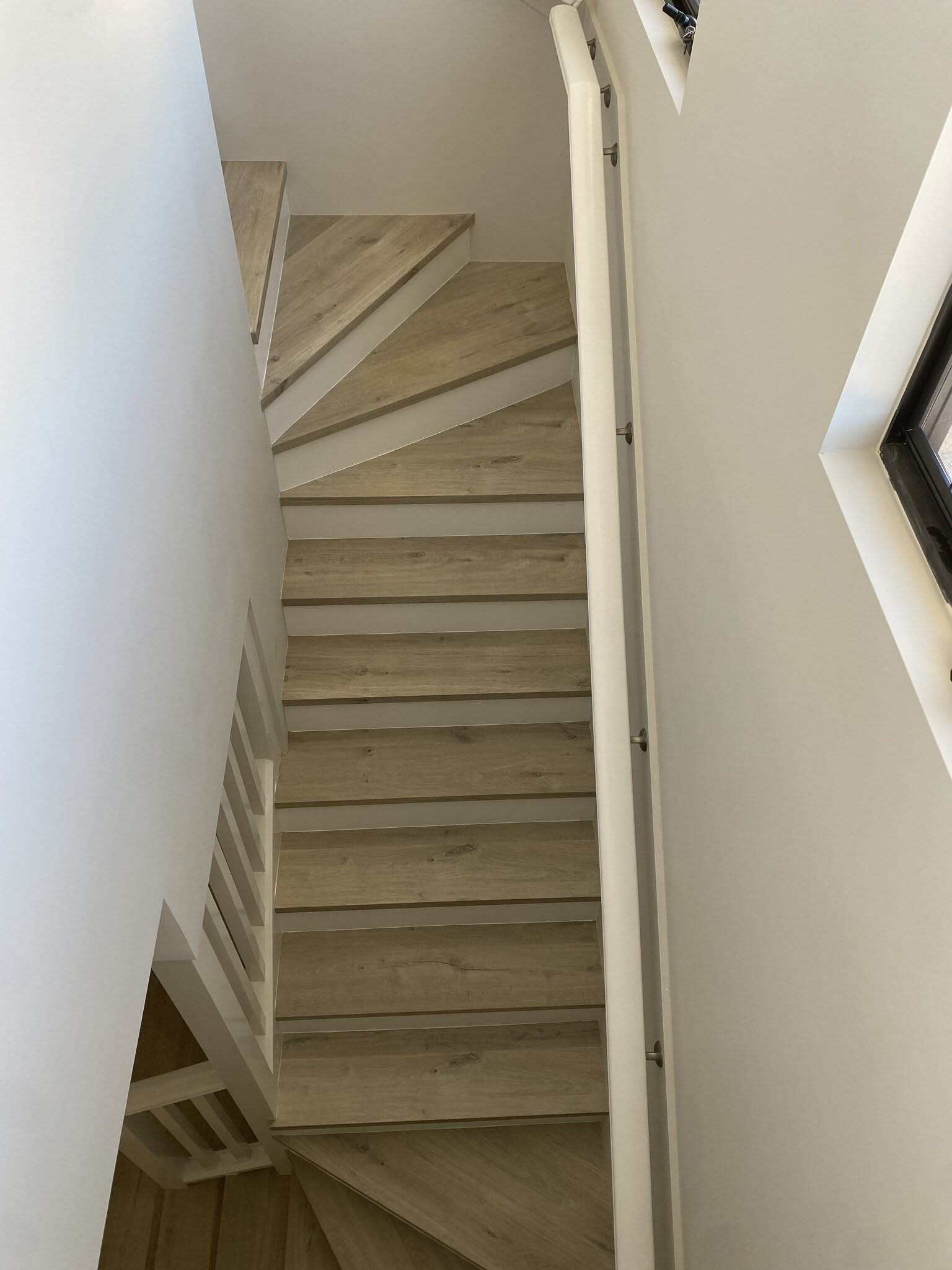 Narrow winding staircase with light treads and white risers, from the top