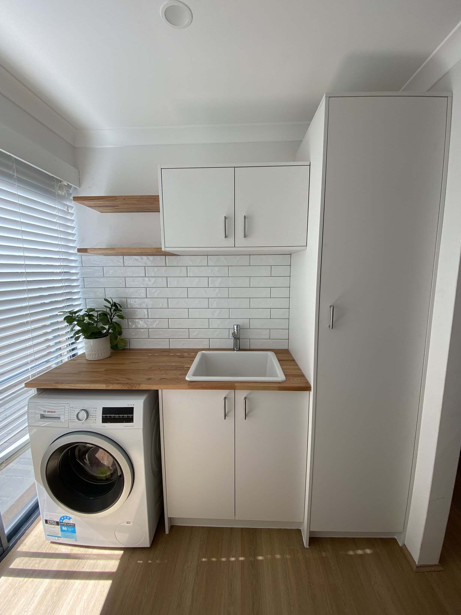 Laundry with white cabinets, tall cupboard, timber benchtop and floating shelves