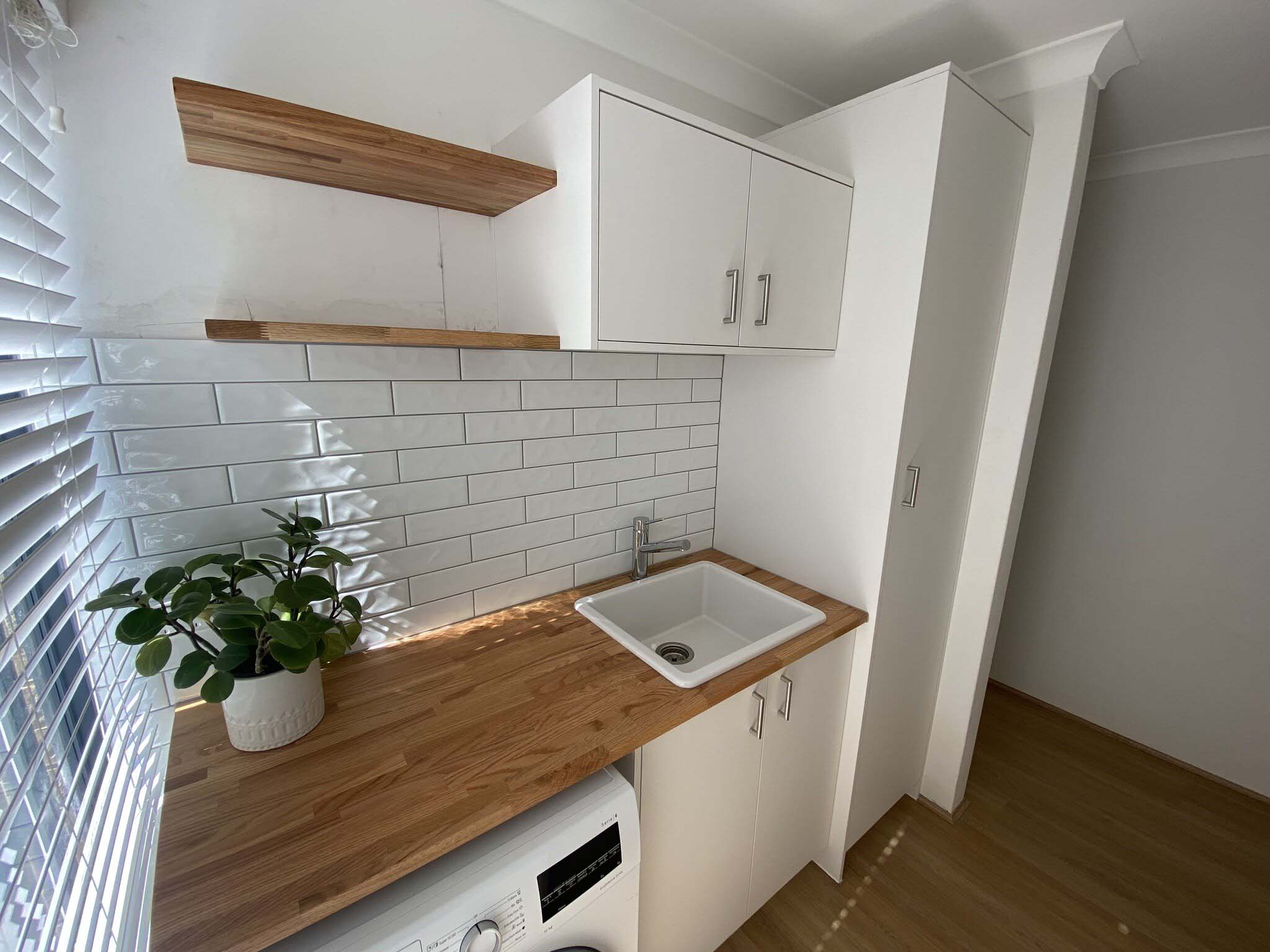 Close view of a laundry with floating timber shelves and white subway tiles