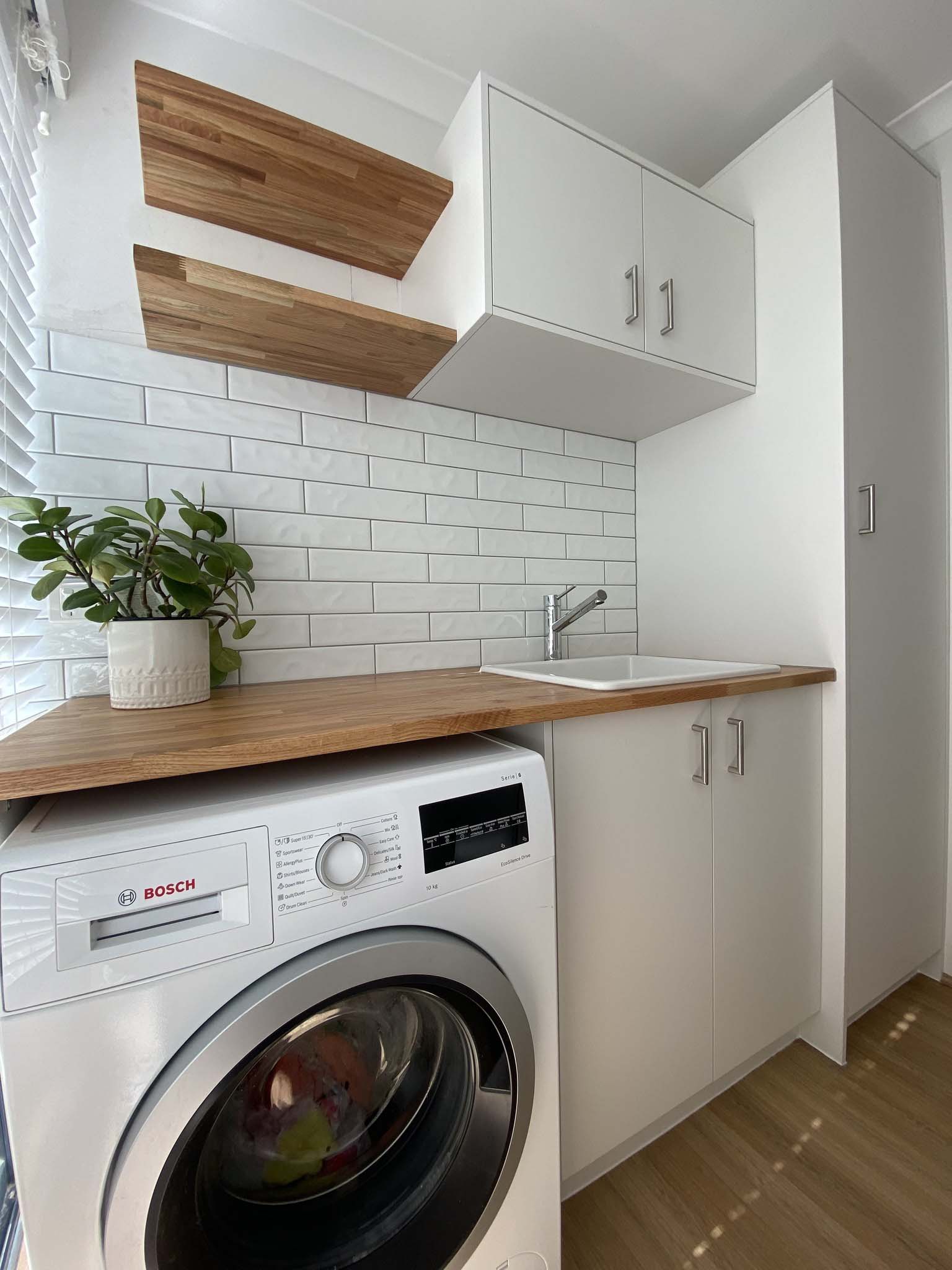 Laundry with white cabinets, timber benchtop, floating shelves and a front-loader