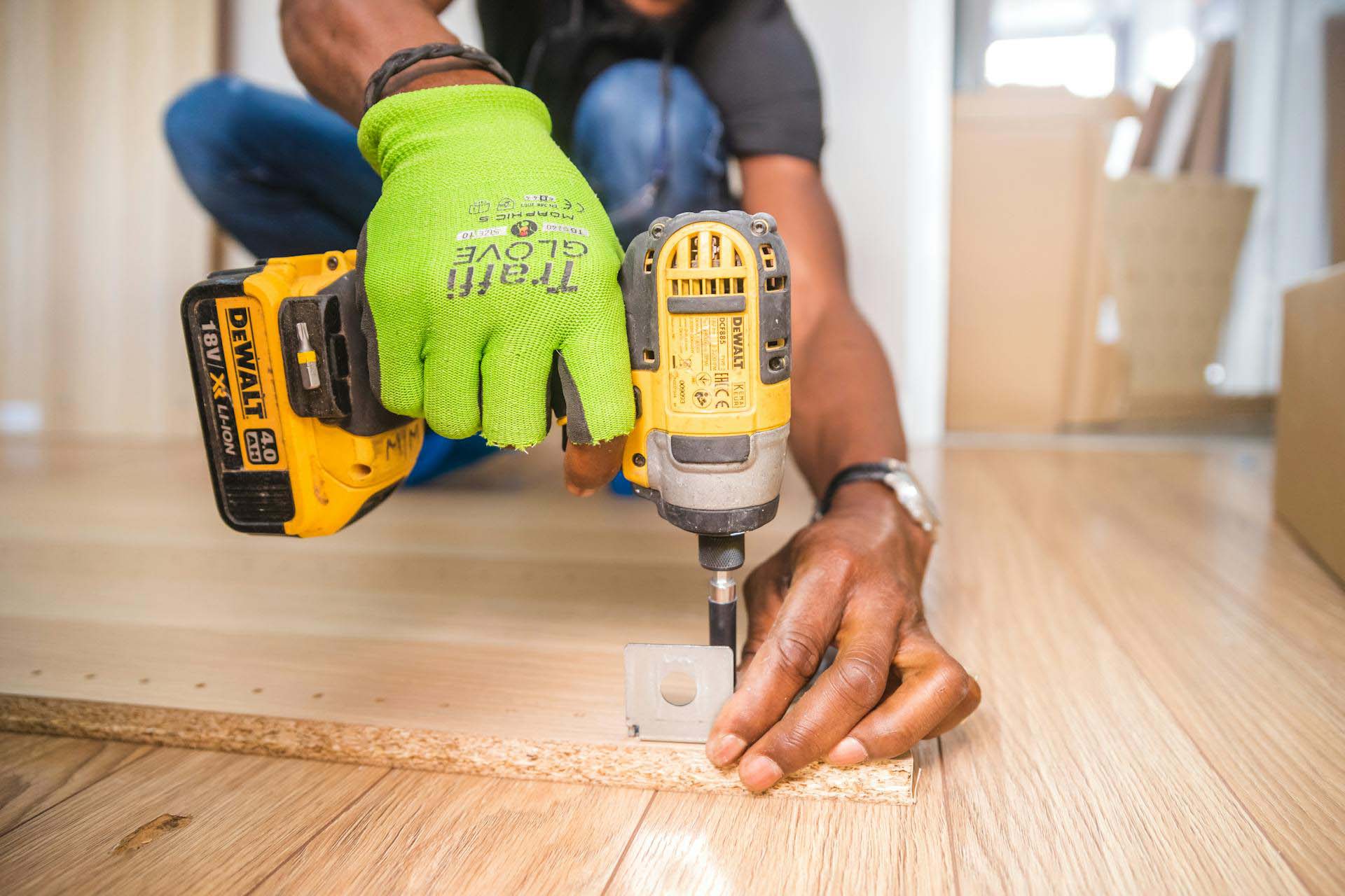 Gloved hands driving a screw into a chipboard panel with a cordless drill