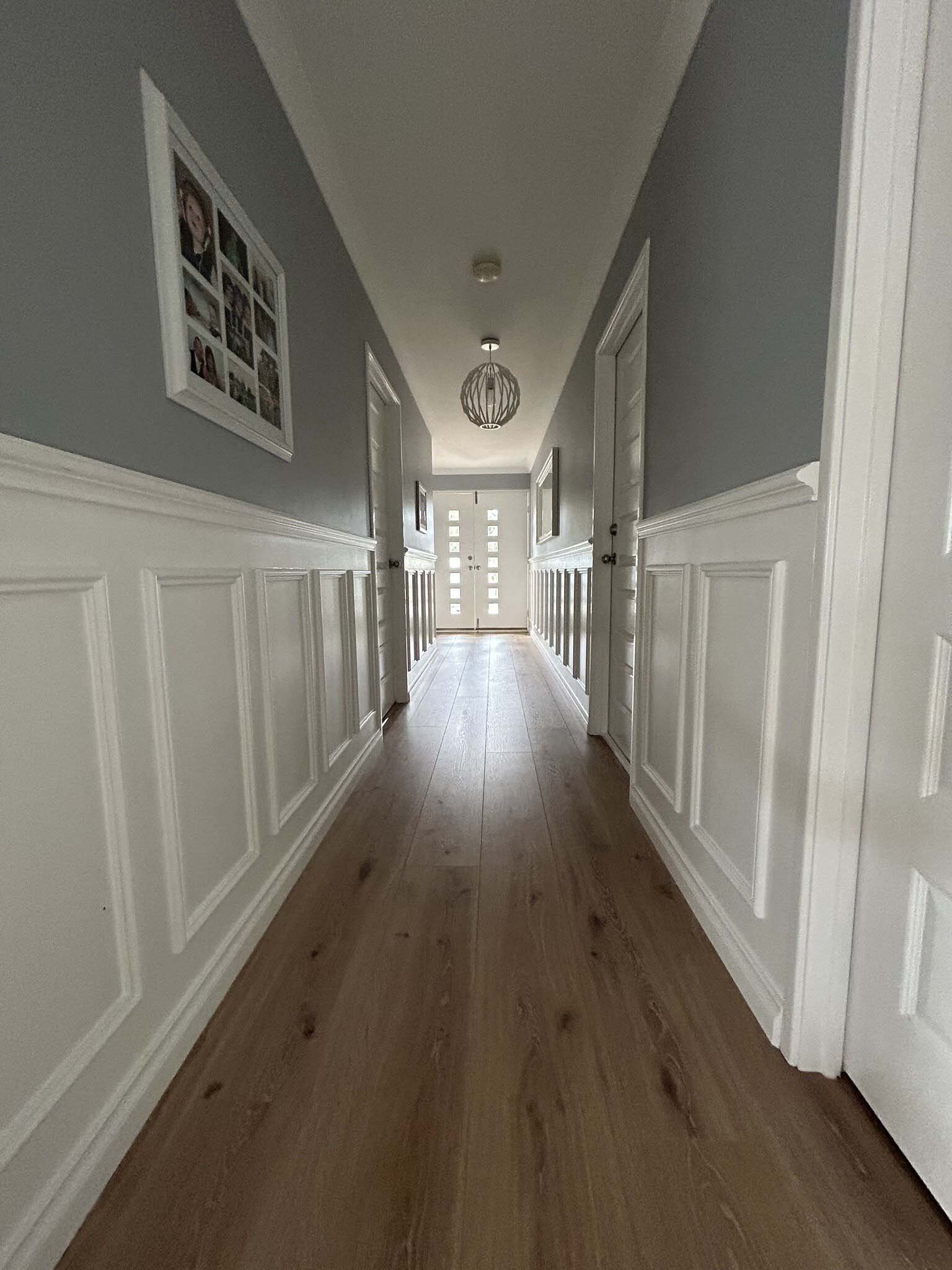 Long hallway with white wainscoting panels and a timber floor