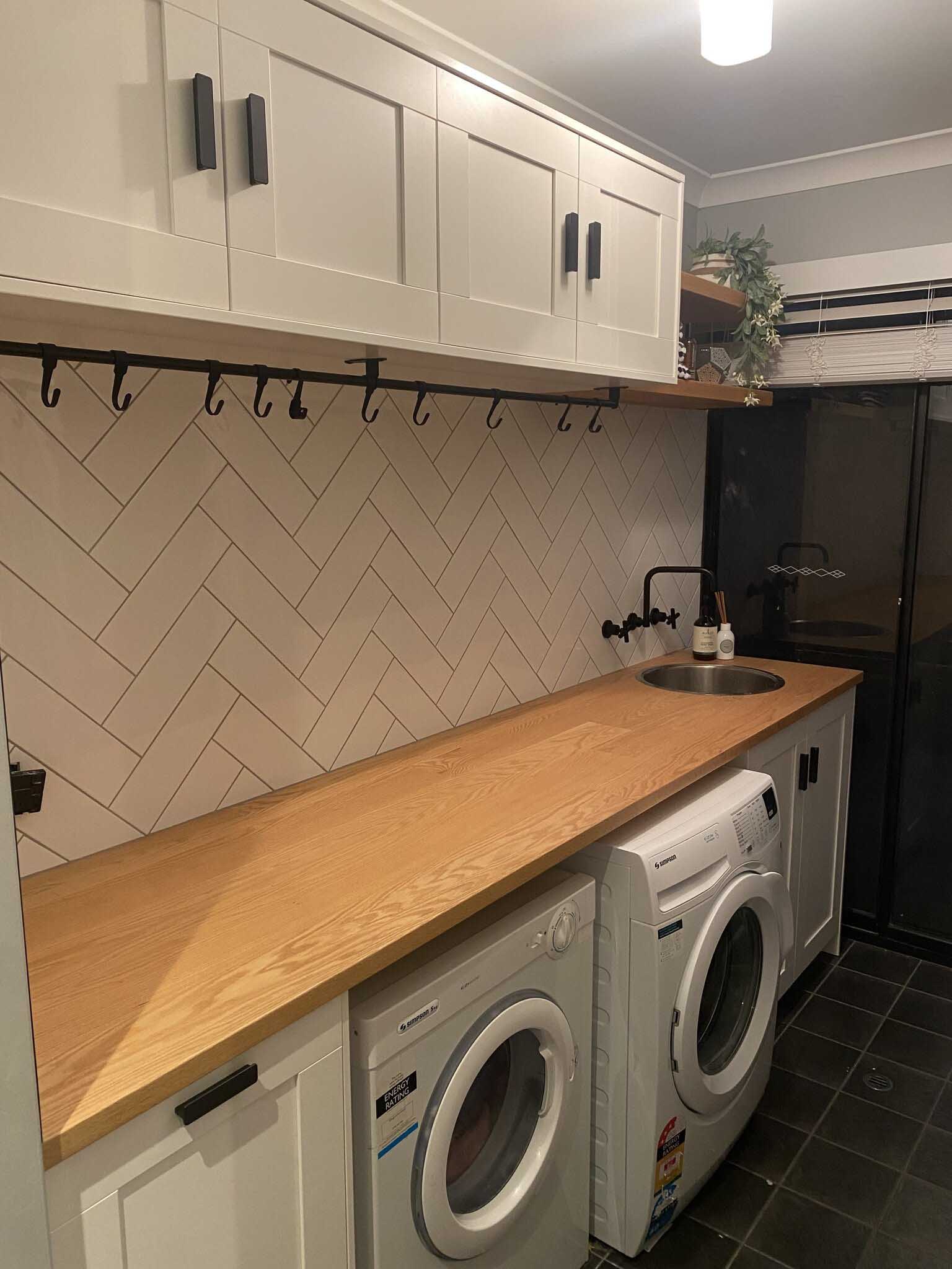 Laundry with a long timber benchtop, herringbone tiles and two machines