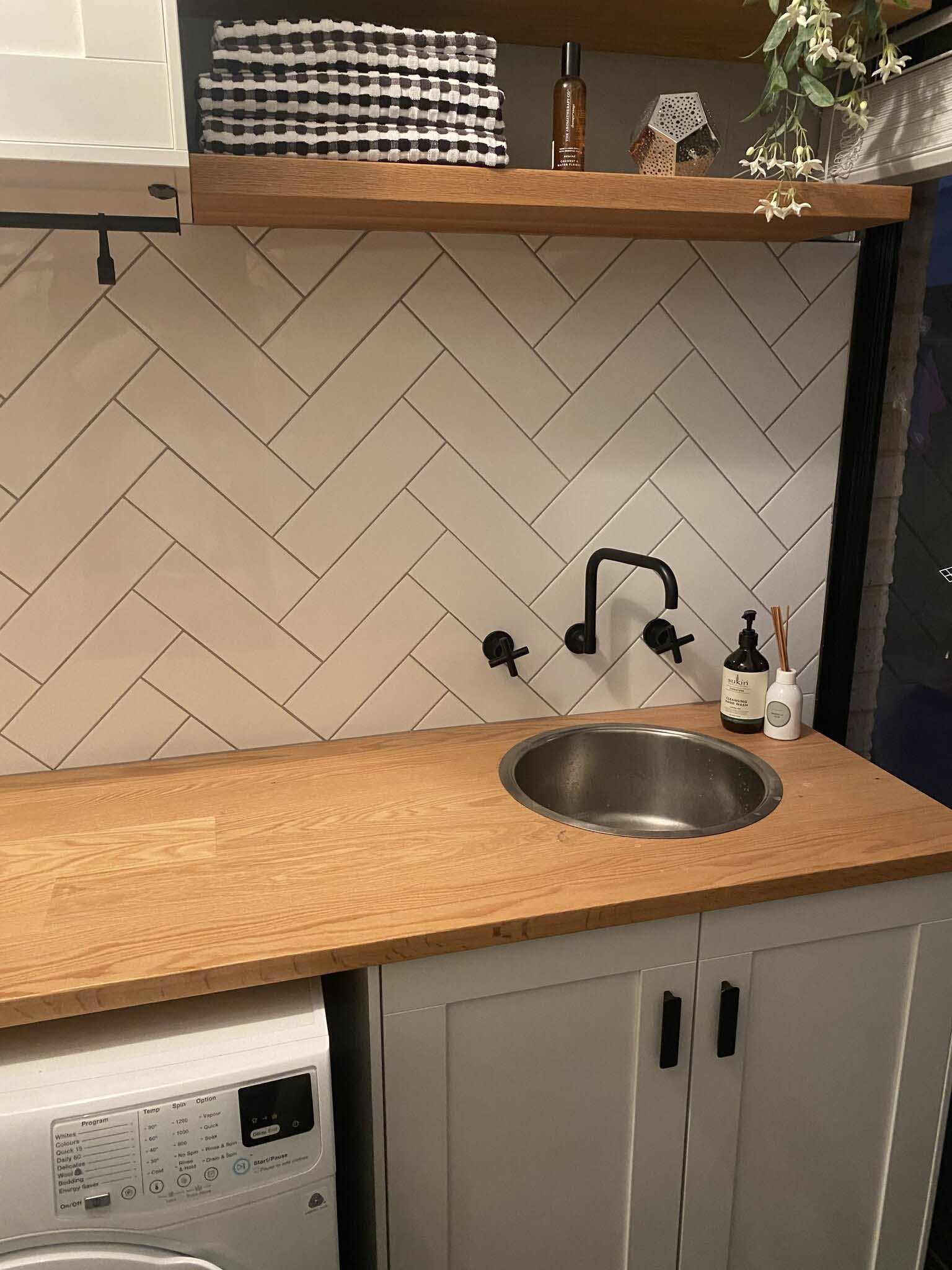 Laundry benchtop with round sink, black tapware and herringbone tiles