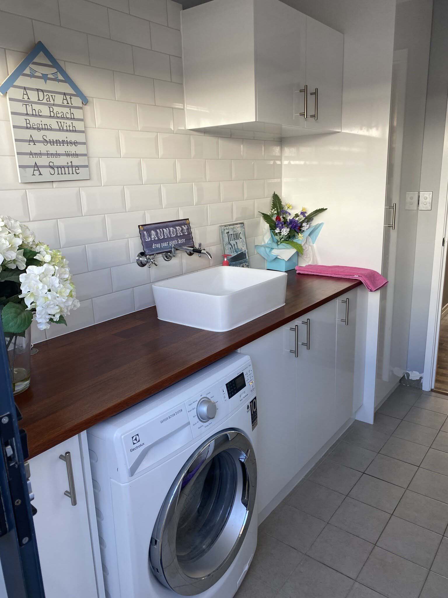 Laundry with dark timber benchtop, white cabinets and white basin