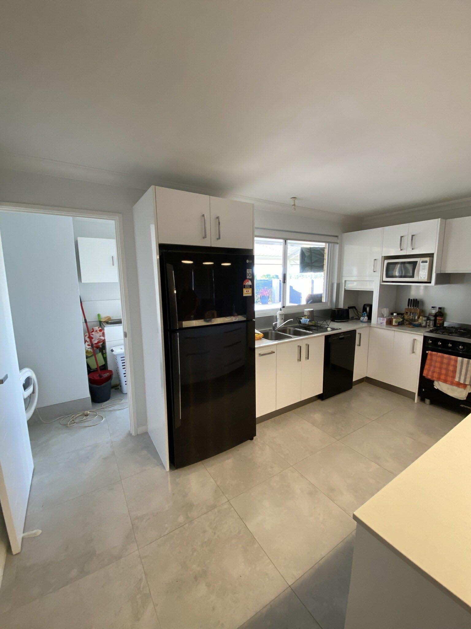 Kitchen with white cabinets, black fridge and grey tiled floor