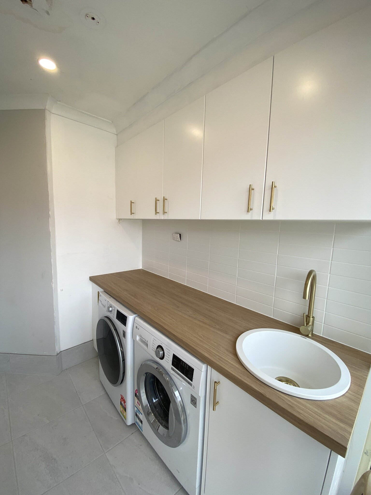Laundry with white overhead cupboards, timber-look benchtop and sink