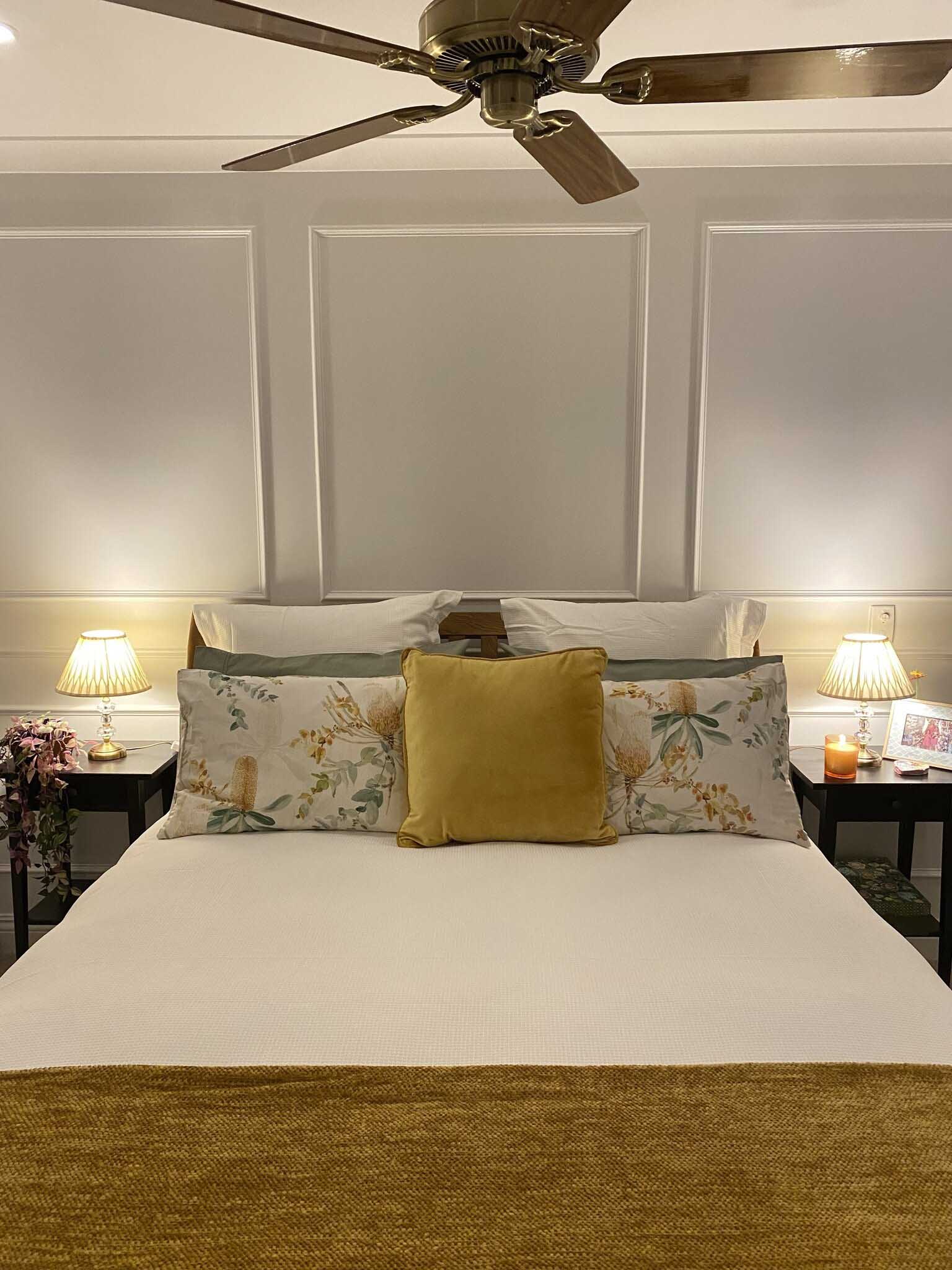 Bed against a wall with white panel moulding, bedside tables and lamps