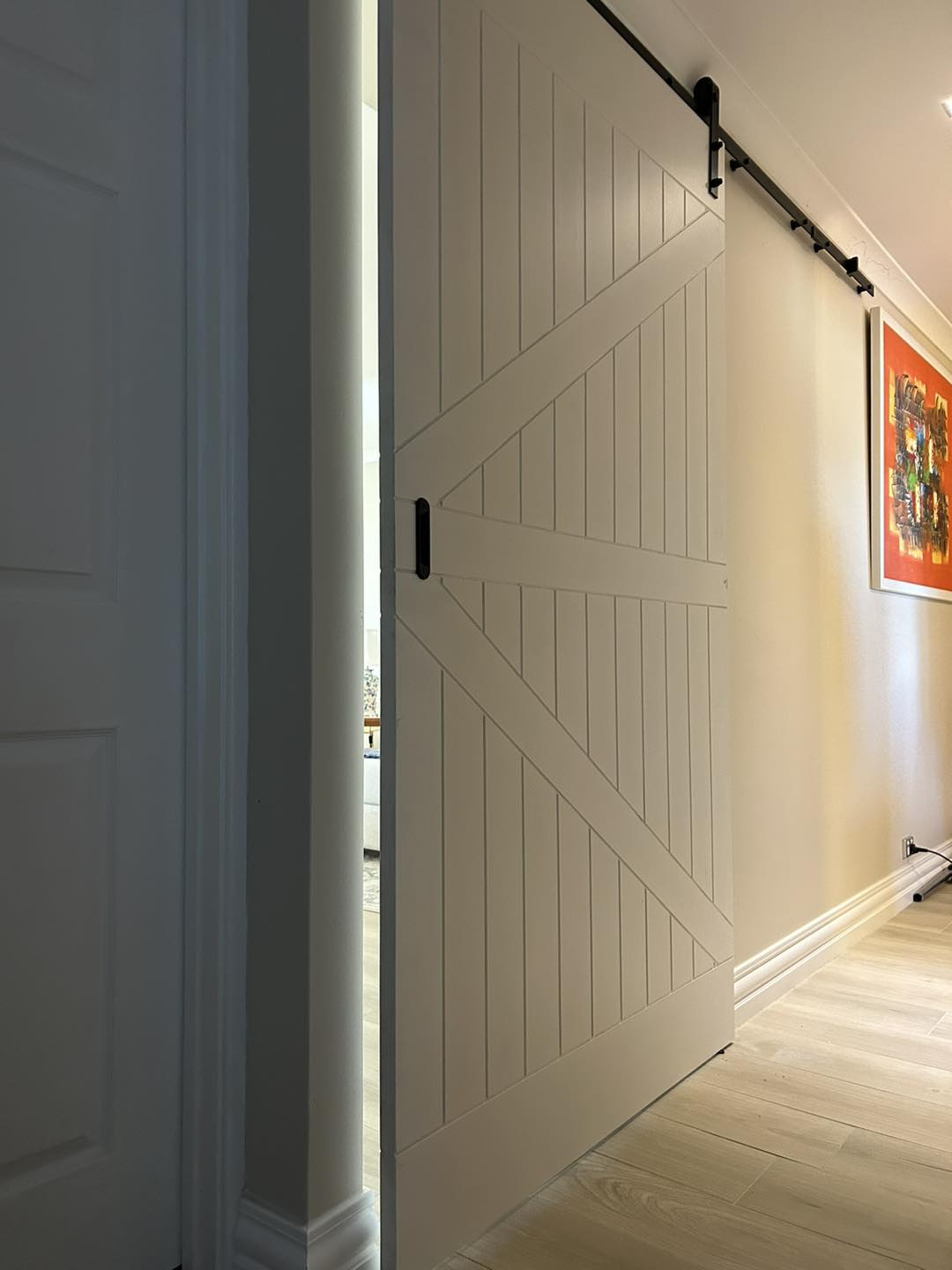 White barn-style sliding door on a black track in a hallway
