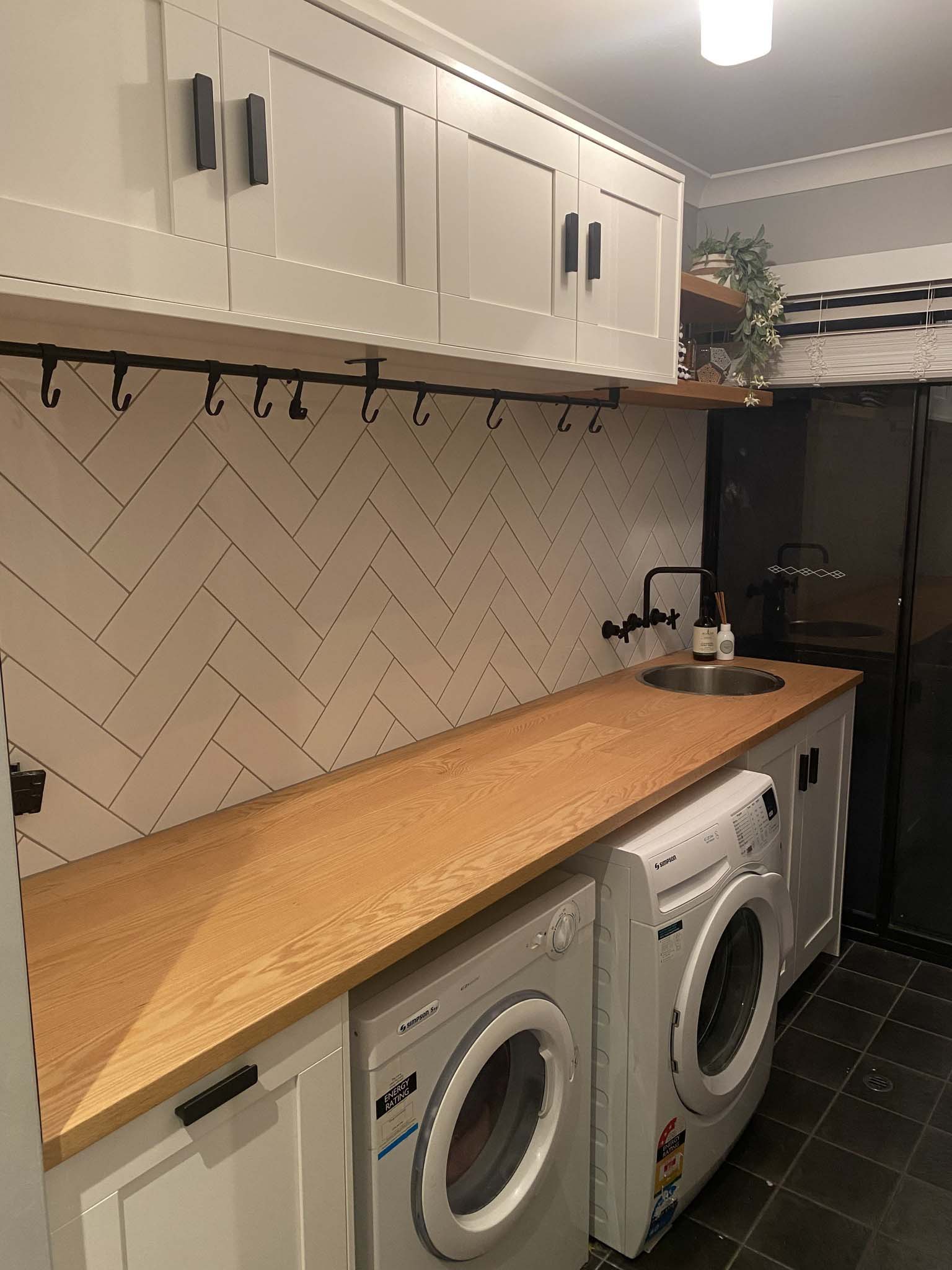 Laundry with white shaker cabinets, timber benchtop and herringbone tile splashback