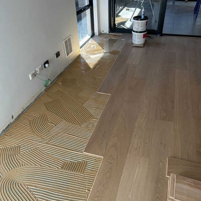 Timber floorboards being laid over adhesive on a concrete floor