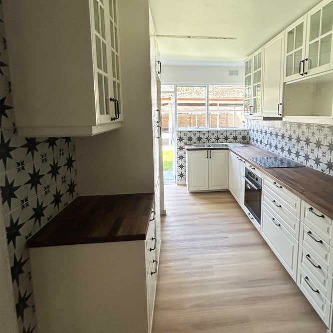 Galley kitchen with white shaker cabinets, timber benchtops and patterned tiles