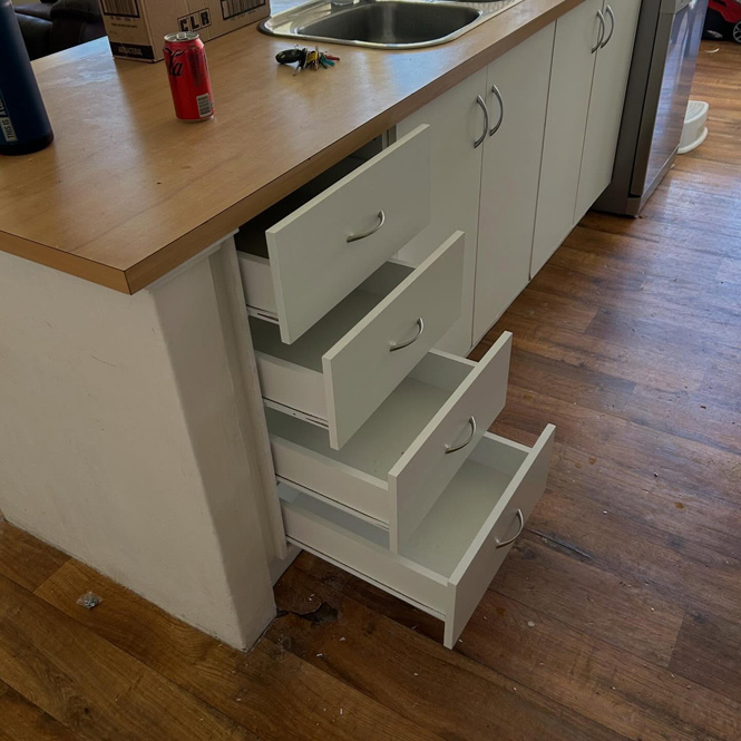 Open white drawers in a kitchen cabinet with a timber benchtop