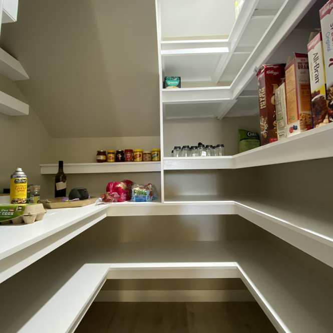 Walk-in pantry with white wraparound shelves and stocked groceries
